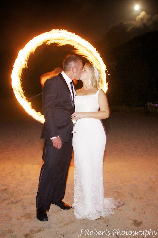 Bride and groom kissing in front of fire dancing ring of fire and full moon - wedding photography sydney